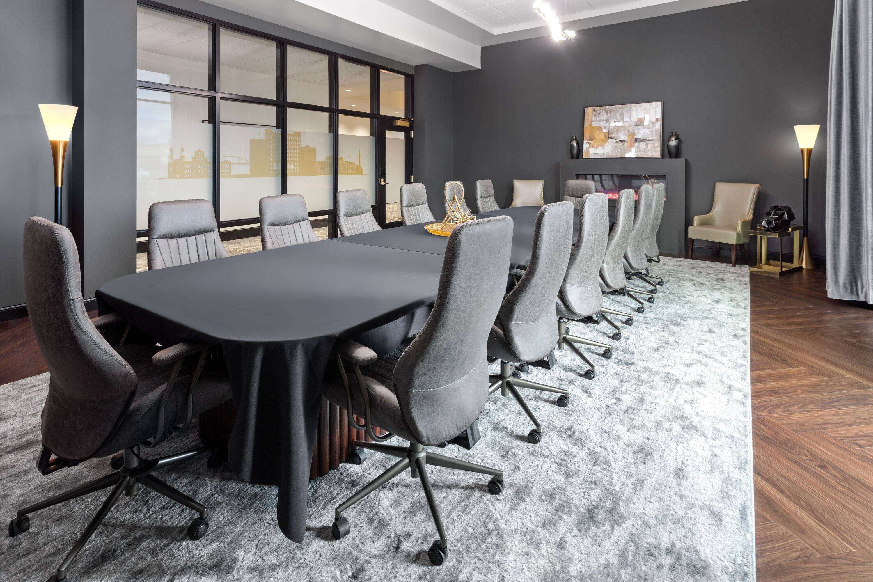 A conference room with a long table, multiple chairs, a fireplace, and large windows.