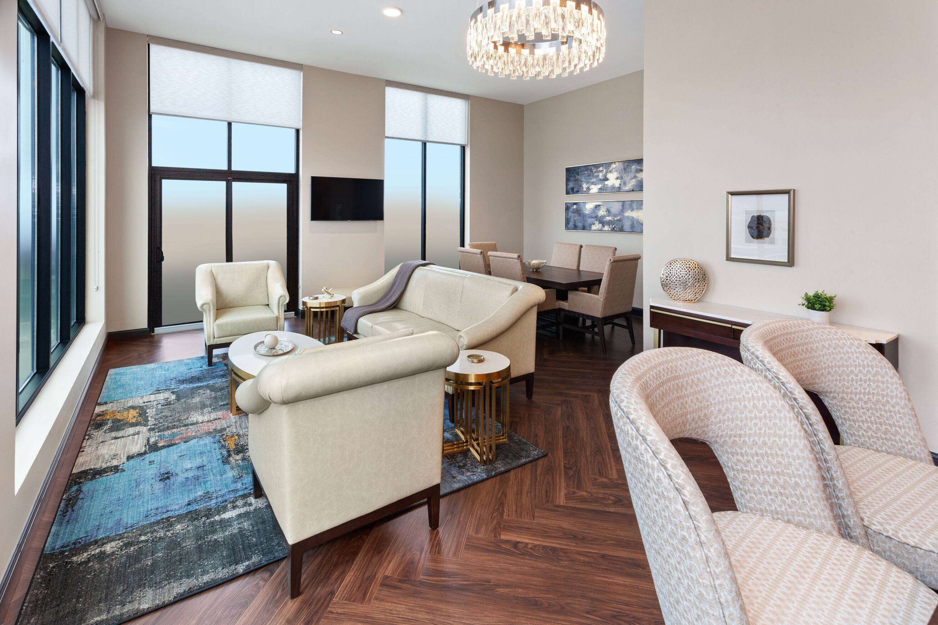 A spacious living area with a large sofa, a smaller sofa, and a chair. There is a dining table with chairs, a TV mounted on the wall, and artwork on the walls.