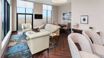 A spacious living area with a large sofa, a smaller sofa, and a chair. There is a dining table with chairs, a TV mounted on the wall, and artwork on the walls.