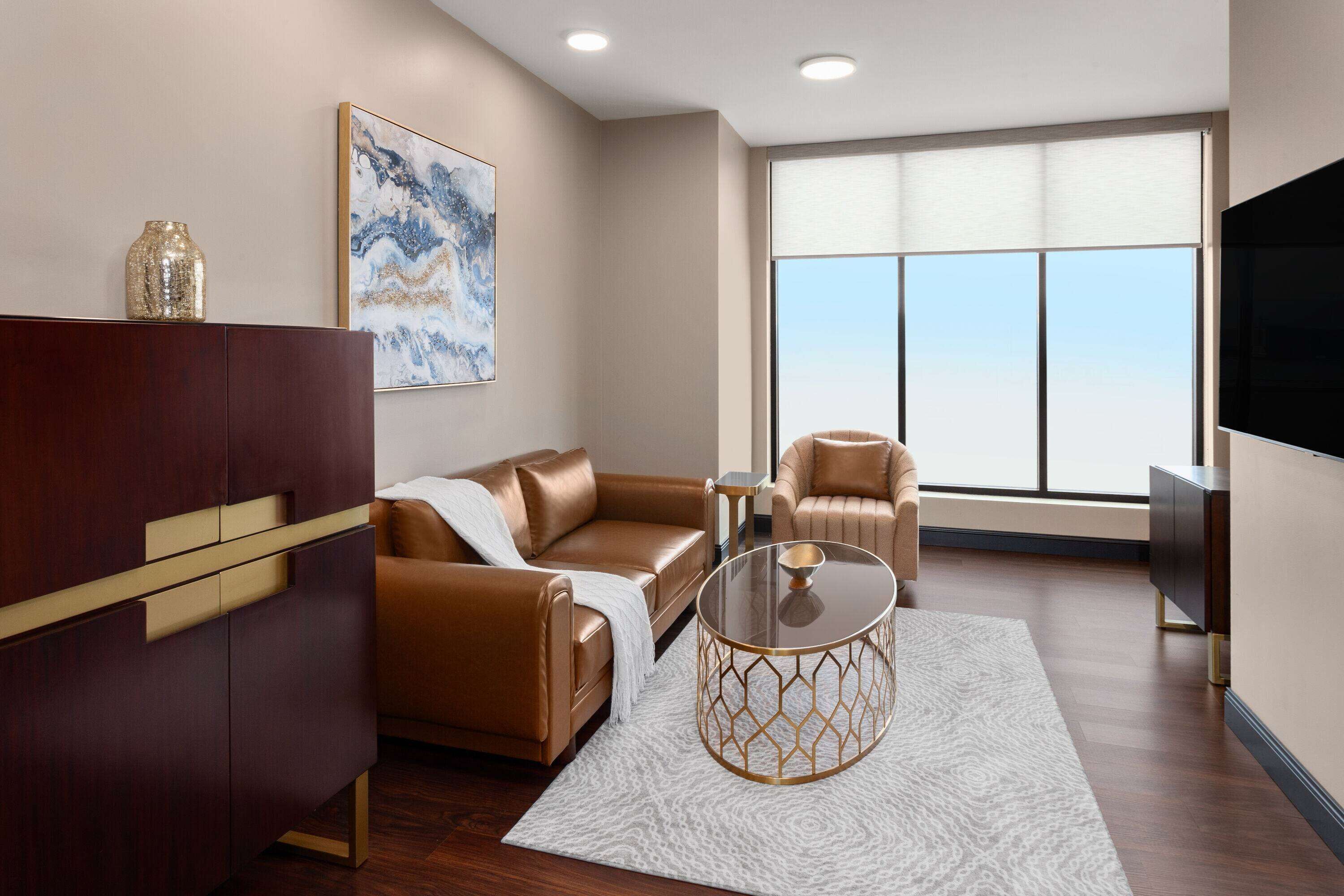 Ein modernes Wohnzimmer mit einer Ledersofa, einem Glastisch und einem großen Fenster mit Blick auf die Stadt.