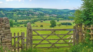 A rustic stone wall and a wooden gate leading to a lush green landscape with rolling hills and a village in the distance. - 2 bedroom accommodation in Eyam, near Bakewell (Eyam, near Bakewell)