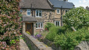 A stone house with a traditional design, featuring a stone wall and a small garden with various flowers. - 2 bedroom accommodation in Eyam, near Bakewell (Eyam, near Bakewell)