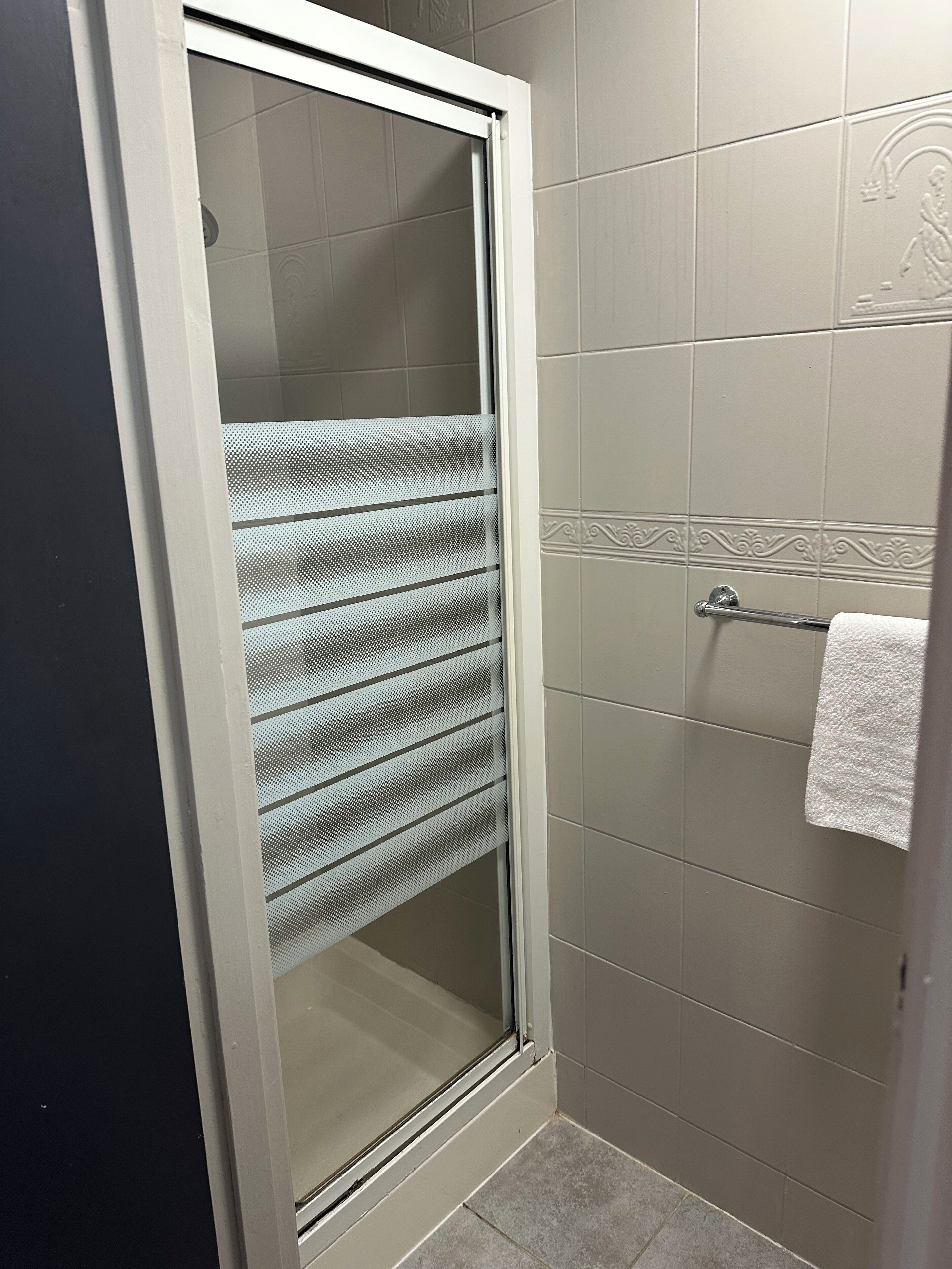 A bathroom with a glass shower door, tiled walls, and a towel rack.