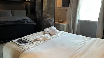 A hotel room with a large bed, a nightstand with a lamp, a bathroom with a mirror, and a view of the outside.