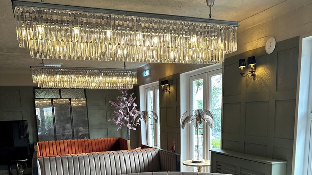 A modern living room with a large curved sofa, a round coffee table, and a decorative chandelier. - The Q Hotel (Shanklin)