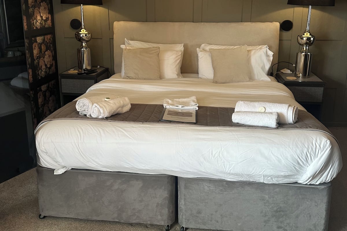 A double bed with two nightstands, each with a lamp, in a room with a wooden ceiling and a floral-patterned wall.