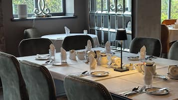 A dining area with a table set for four, including plates, cutlery, and glasses. There are chairs around the table, and a window with a view of greenery outside.