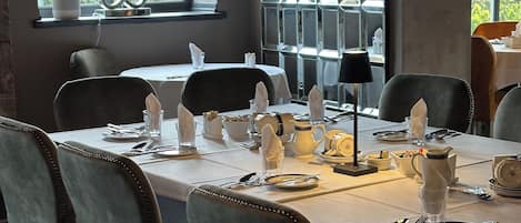 A dining area with a table set for four, including plates, cutlery, and glasses. There are chairs around the table, and a window with a view of greenery outside.