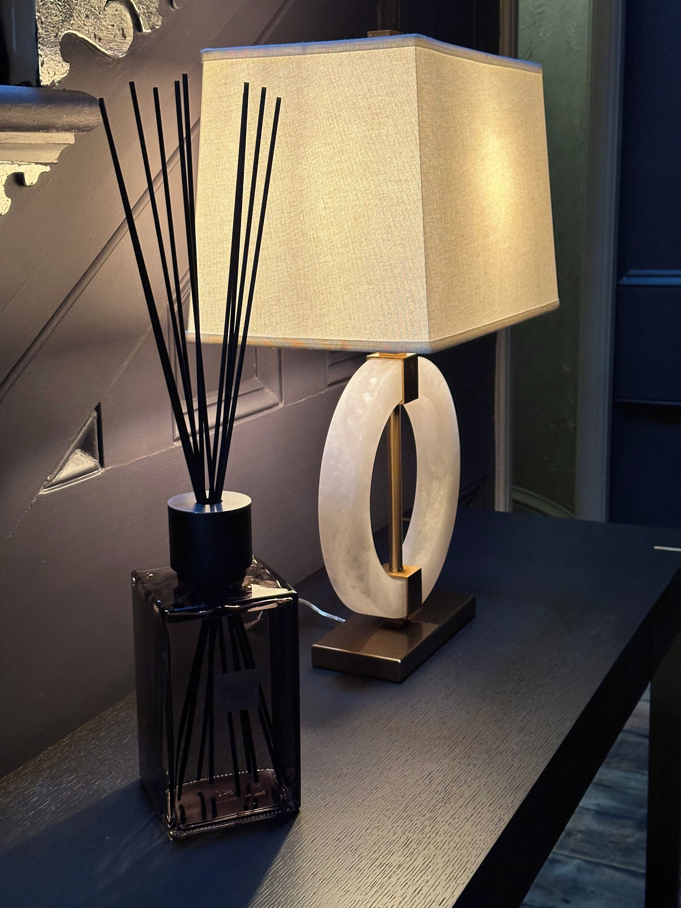 Une table moderne agrémentée d’une lampe décorative et d’un vase noir contenant des tiges de roseau.