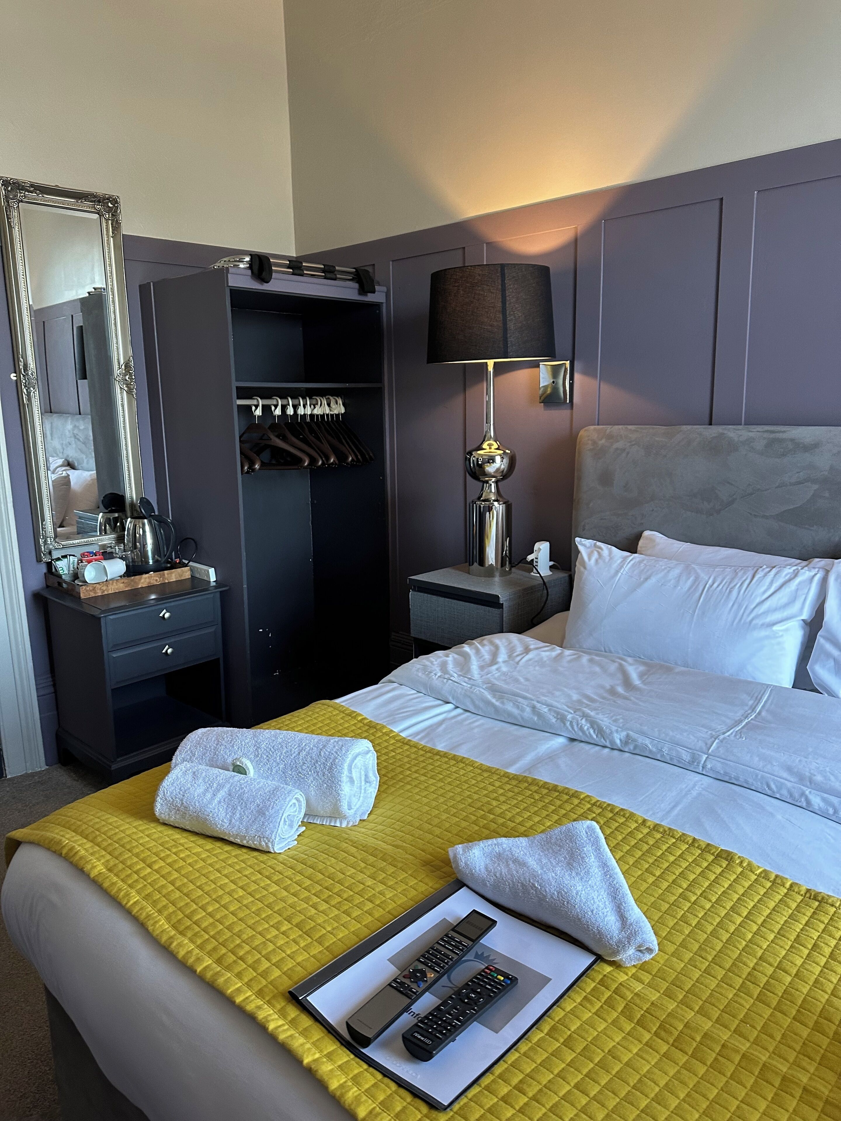 A hotel room with a bed, a bedside table, a lamp, a wardrobe, and a mirror.