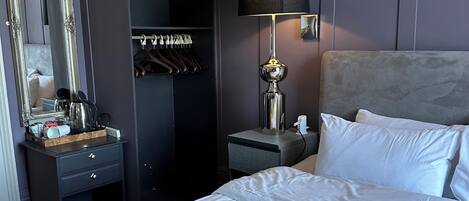 A hotel room with a bed, a bedside table, a lamp, a wardrobe, and a mirror.