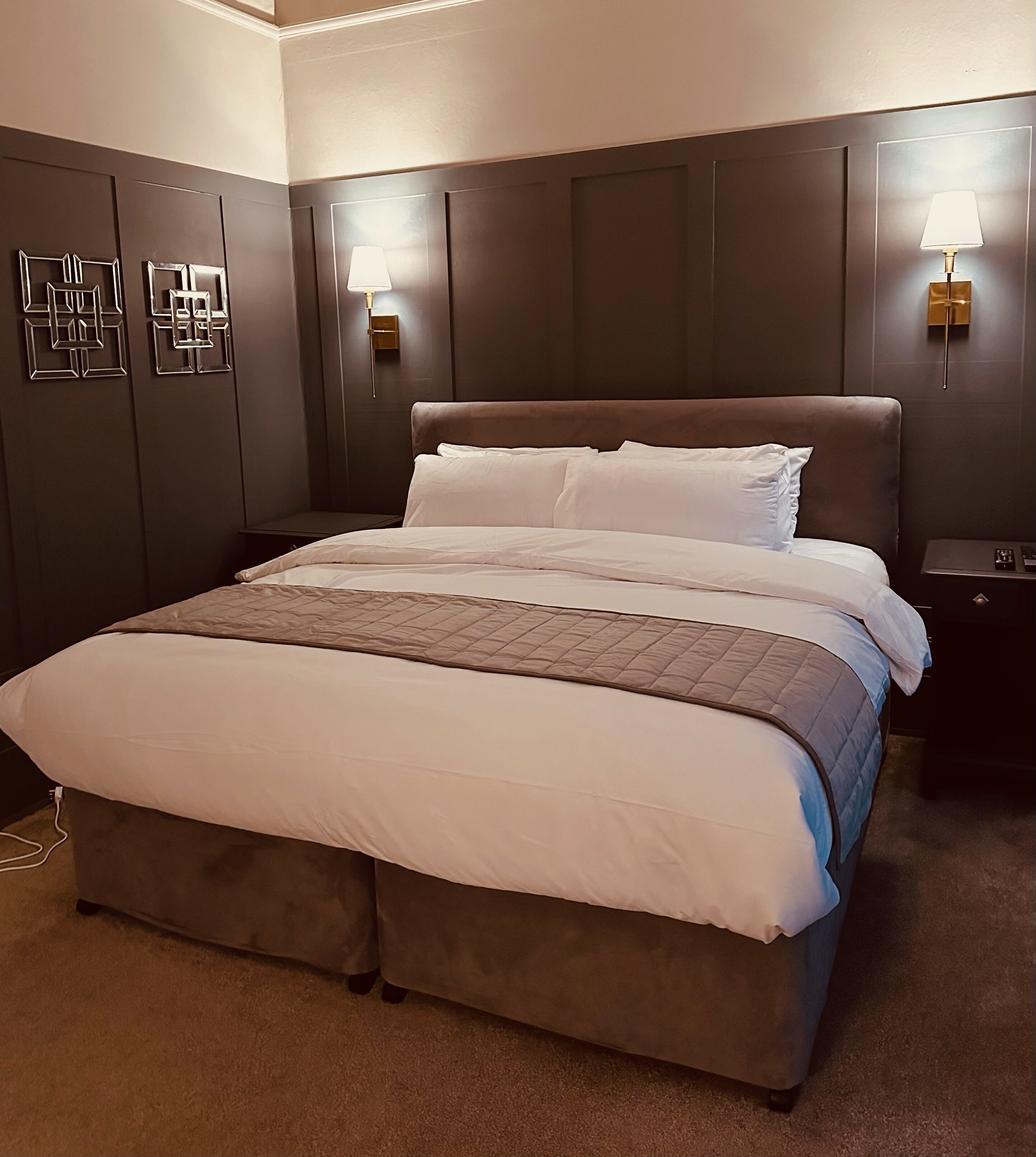 A neatly made bed with a quilted headboard, two bedside tables with lamps, and wall-mounted light fixtures.