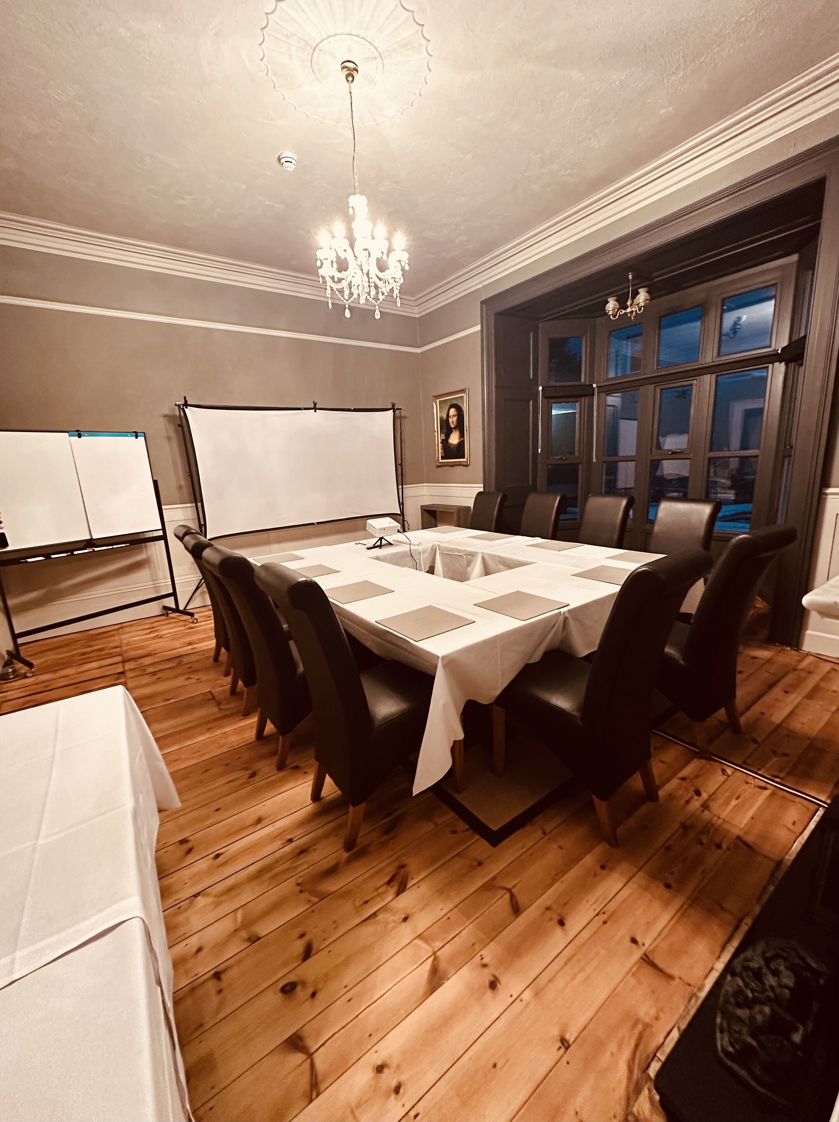 A conference room with a large table, chairs, a whiteboard, and a chandelier.