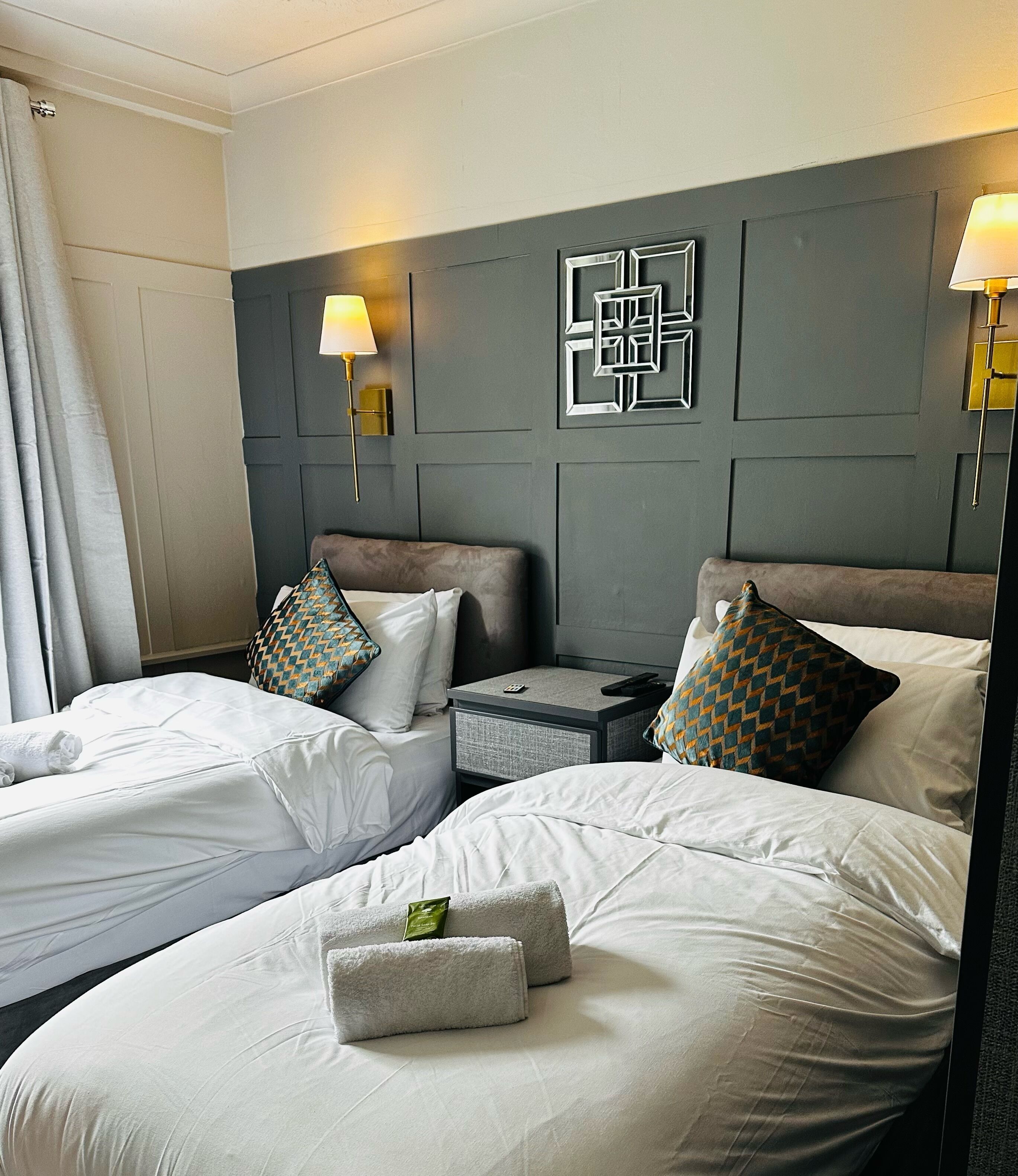 A hotel room with two beds, a bedside table, a lamp, and a wall decoration.