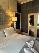 Une chambre d’hôtel avec un lit, une table de chevet avec une lampe, un miroir et un mur orné d’un tableau.