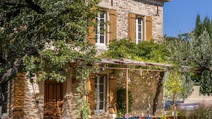 Un edifici de pedra amb teulada de rajola, mobiliari exterior i un arbre al primer pla.