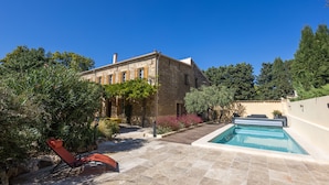 Edifici de pedra amb una piscina, envoltat de verdura i un cel blau clar.
