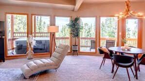 A spacious living area with large windows, a comfortable chair, a dining table with chairs, and a chandelier. - *NEW* Stunning Mountain Views/Hot Tub/3BR/Sleeps 6 (Fairplay)