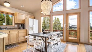 A modern kitchen with wooden cabinets, a dining table with chairs, and large windows offering a view of the outdoors. - *NEW* Stunning Mountain Views/Hot Tub/3BR/Sleeps 6 (Fairplay)