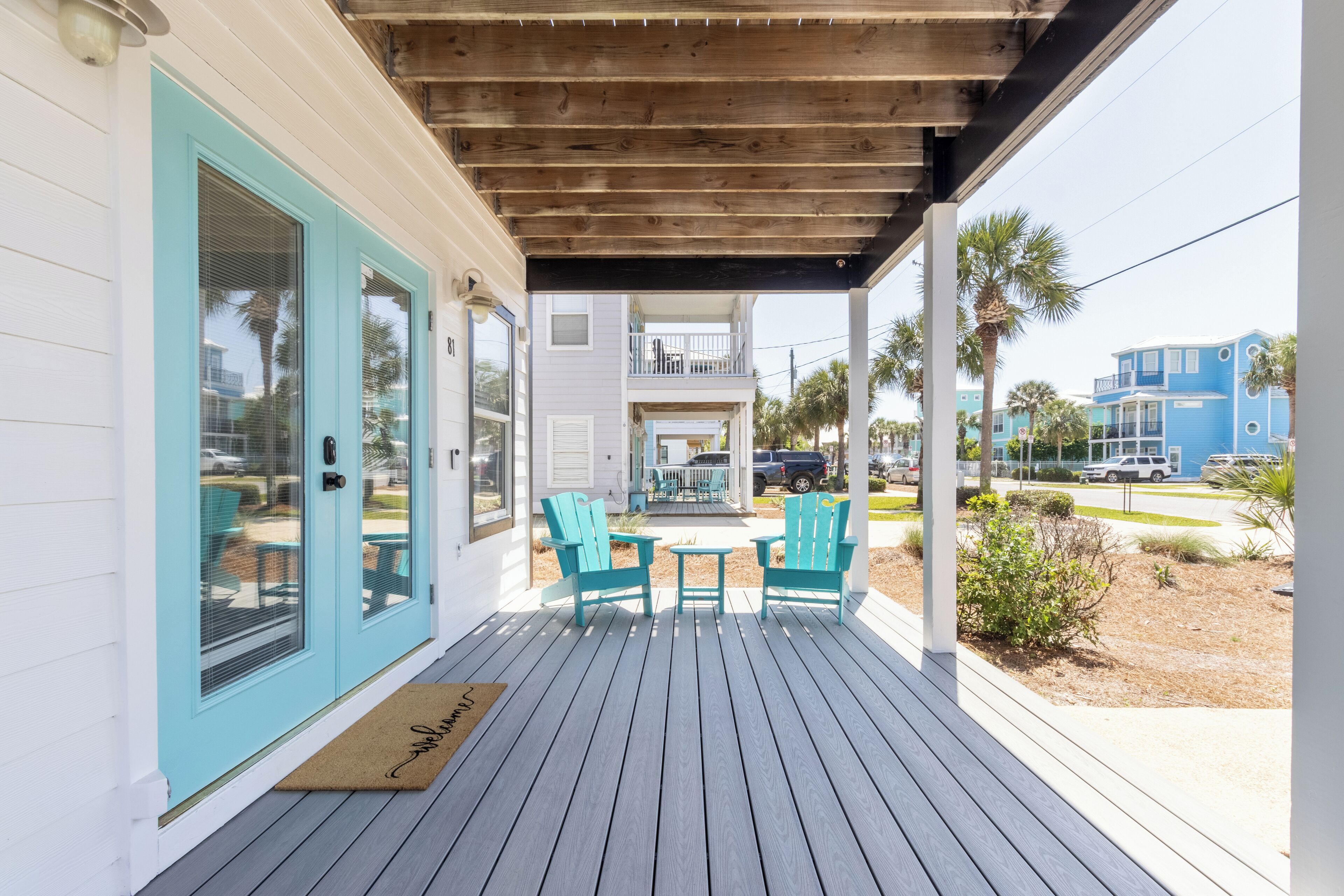 A covered porch with a wooden ceiling, turquoise doors, and matching chairs.