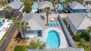 A residential area with multiple houses, each featuring a swimming pool, surrounded by palm trees and a wooden fence. - Home & Cabana House | Pool | Steps to the Beach! (Destin)