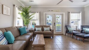 A spacious living room with a brown leather sofa, a wooden coffee table, and two leather armchairs. A ceiling fan is visible, and there is a large potted plant. - Home & Cabana House | Pool | Steps to the Beach! (Destin)