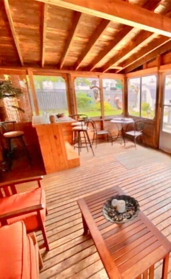 A covered patio area with wooden flooring, a bar counter, and seating arrangements. - On Pointe! (Pointe-du-Chêne)