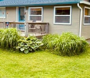A single-story house with a front porch, a small deck, and a well-maintained lawn. - On Pointe! (Pointe-du-Chêne)
