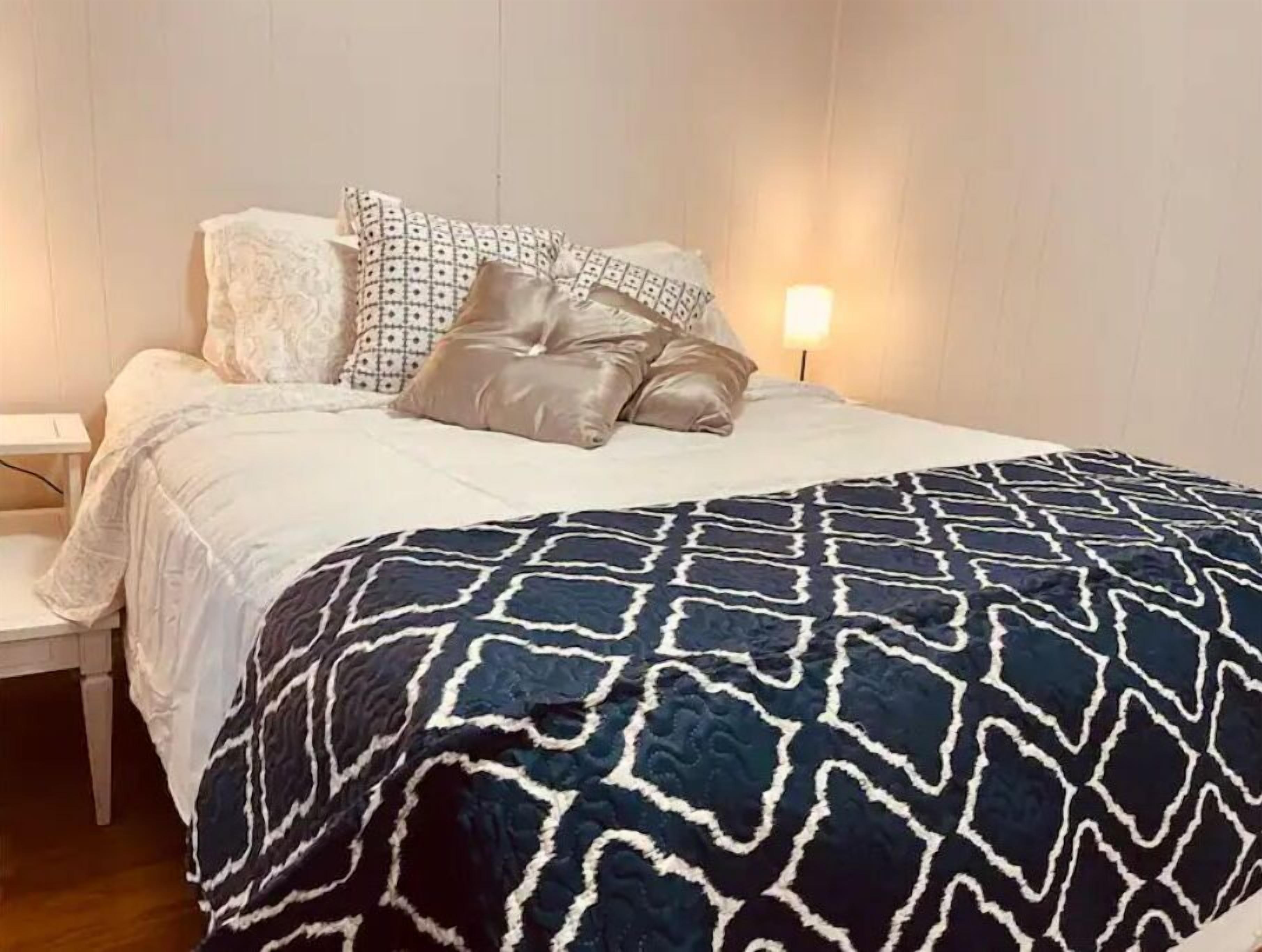 A neatly made bed with patterned pillows and a dark blue geometric blanket.