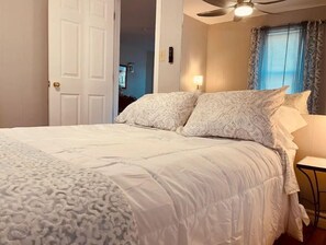 A bedroom with a bed, a ceiling fan, a window with curtains, and a door. - On Pointe! (Pointe-du-Chêne)