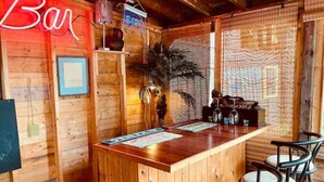 Un coin bar en bois, agrémenté d’un panneau néon, d’une plante et d’un tableau affichant le menu.