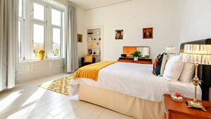 Et hotelværelse med en stor seng, et natbord med lampe, en reol og et vindue med gardiner.