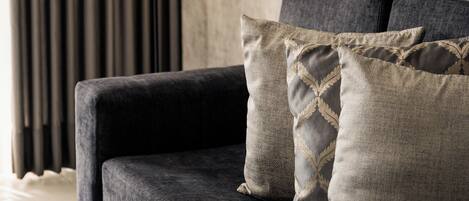 Una sala de estar moderna con un sofá gris oscuro, dos almohadones decorativos, un espejo redondo y una lámpara de pie.