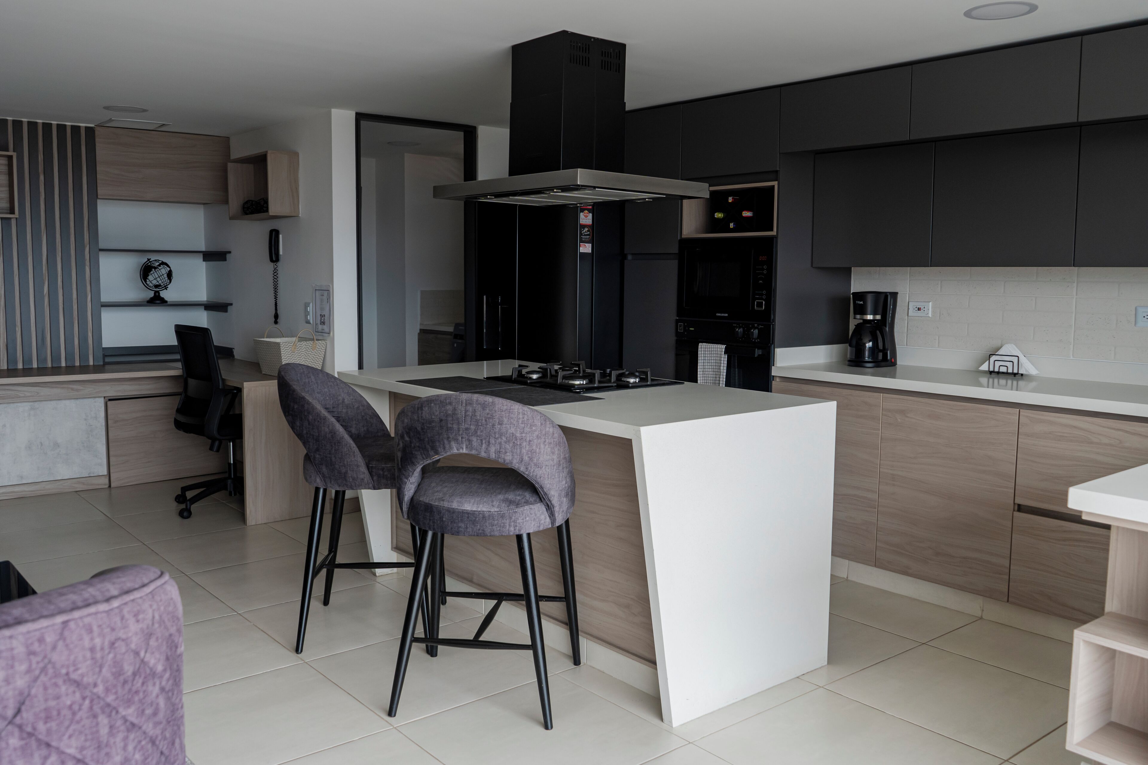 A modern kitchen with a central island, bar stools, a microwave, and a coffee maker.