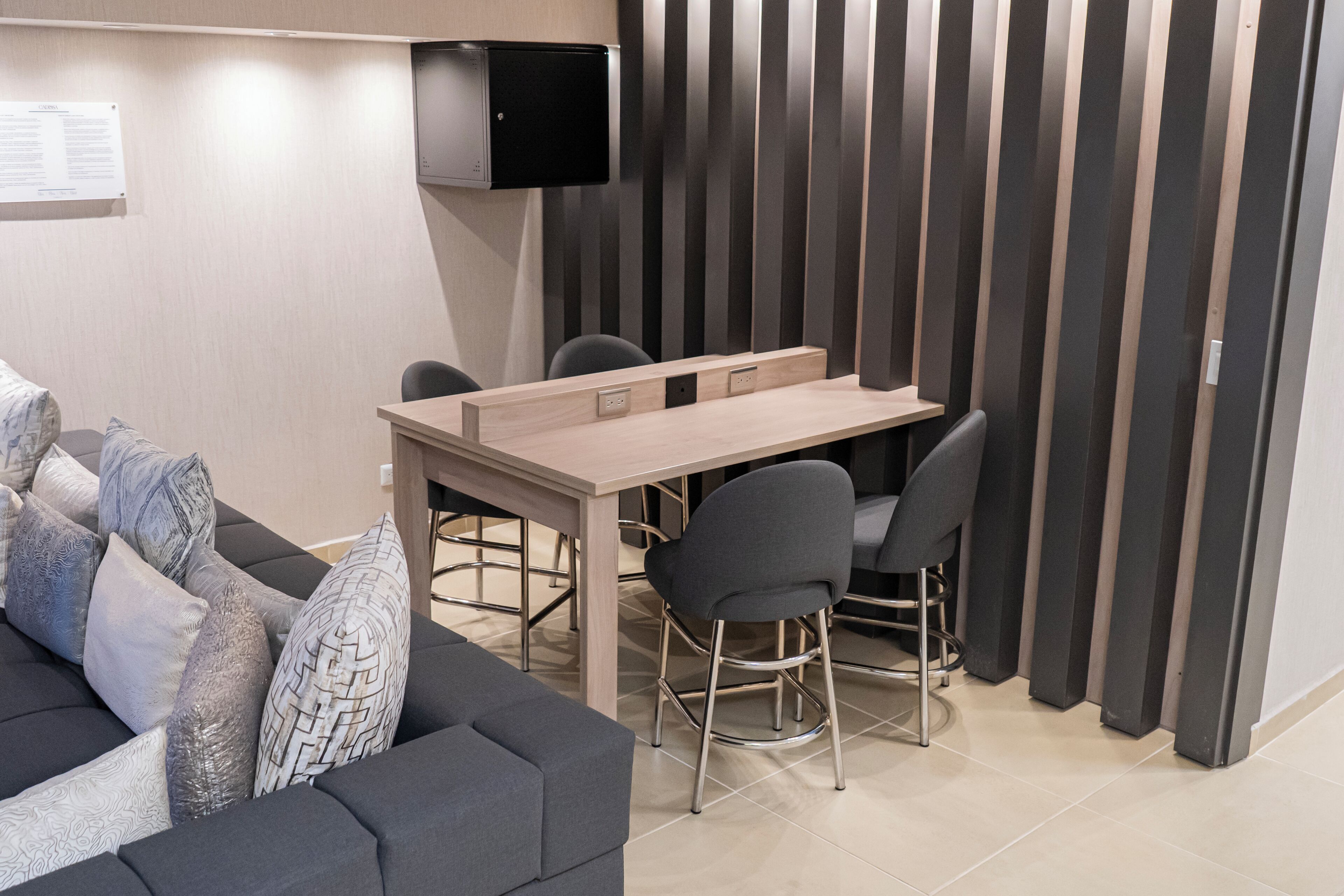 A modern room with a sofa, a dining table with chairs, a TV mounted on the wall, and a partition with vertical slats.