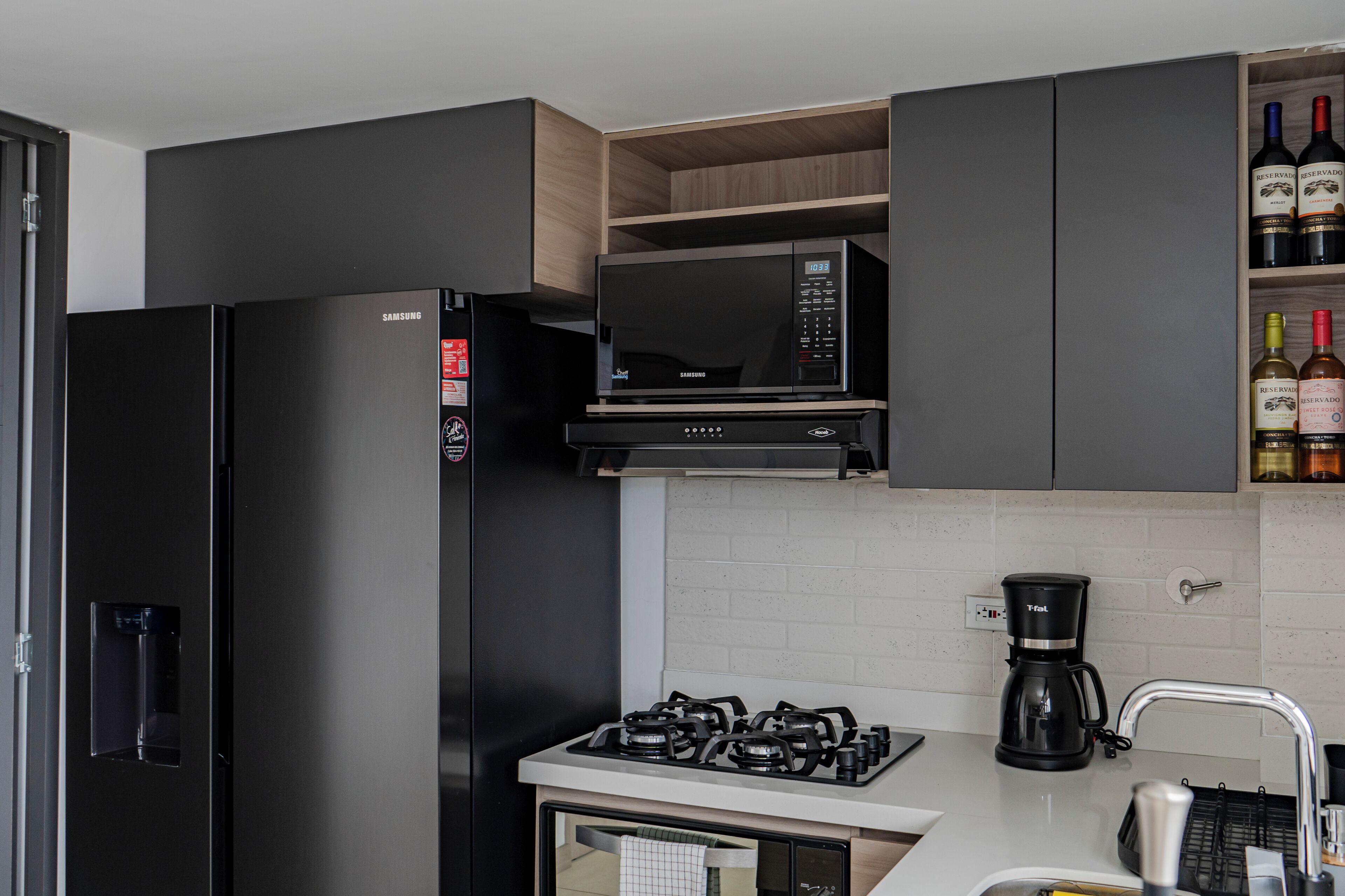 Une cuisine moderne équipée d’un réfrigérateur noir, d’un four à micro-ondes, d’une cuisinière à gaz et d’une machine à café.