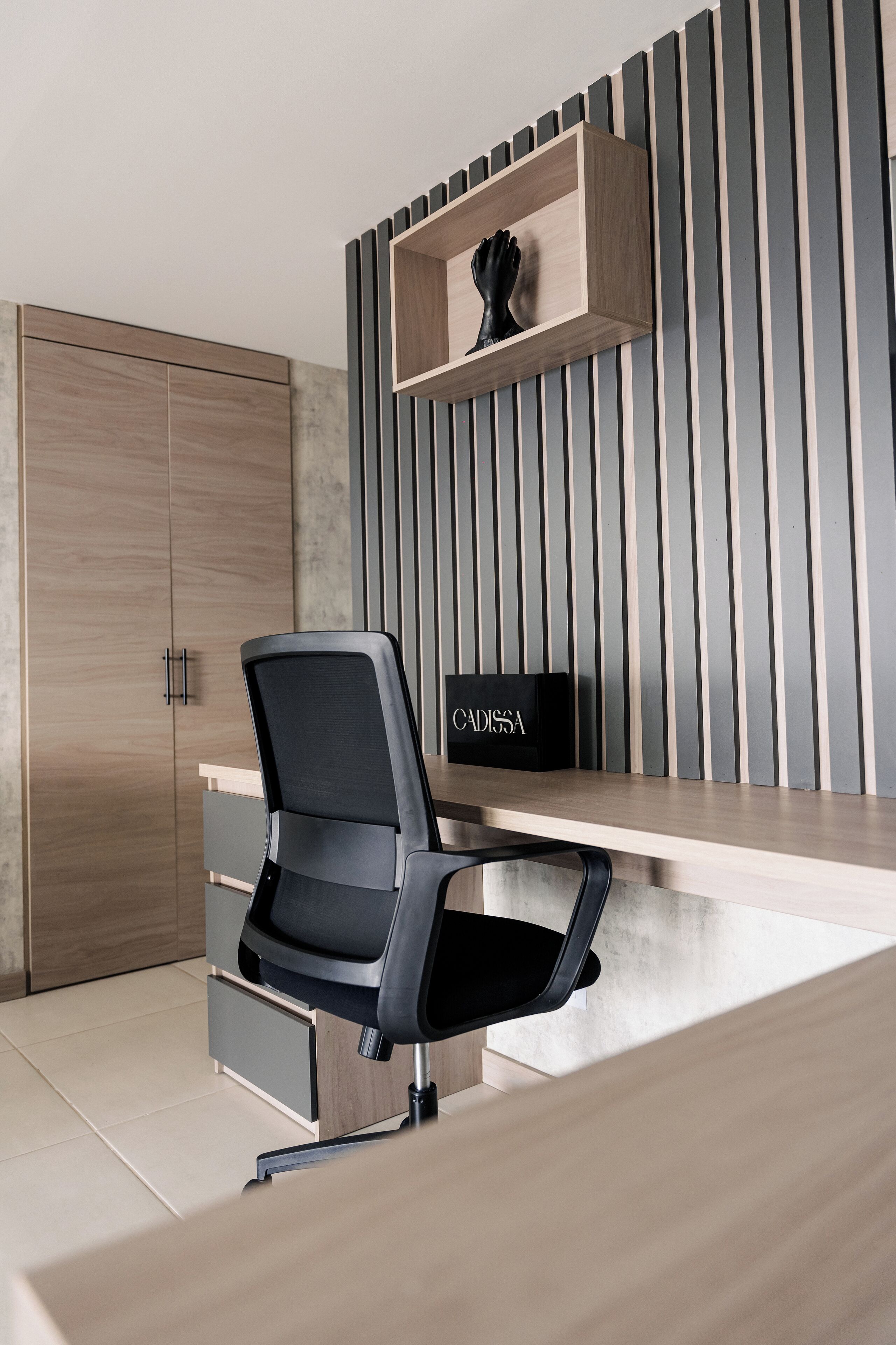A modern office space with a wooden desk, a black office chair, a wooden wardrobe, and a vertical striped wall.