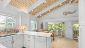 Una cocina moderna con armarios blancos, techo de madera y vista a un patio.