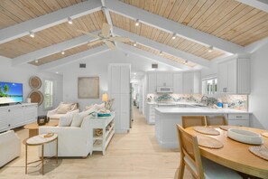 A spacious living area with a white sofa, a wooden dining table, and a kitchen with white cabinets and a tiled backsplash. - Wait and Sea! Amazing location! (Captiva)