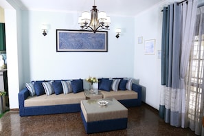 A living room with a blue sofa, a glass coffee table, and a chandelier.
