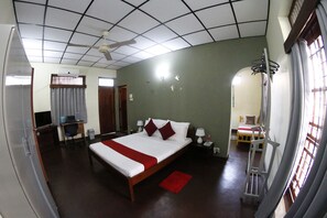 A hotel room with a large bed, a desk, a chair, a TV, and a window with blinds.