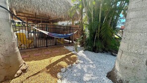 A hammock tied between two concrete pillars, a thatched-roof structure, and a palm tree.