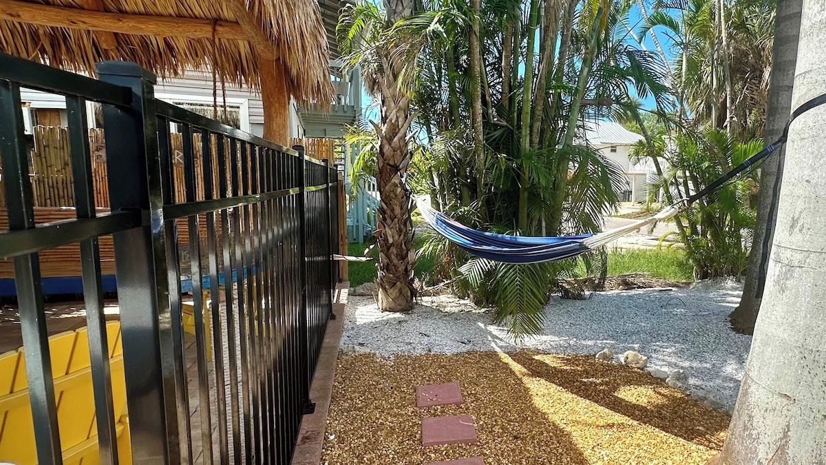 A fenced outdoor area with a hammock, palm trees, and a gravel path.