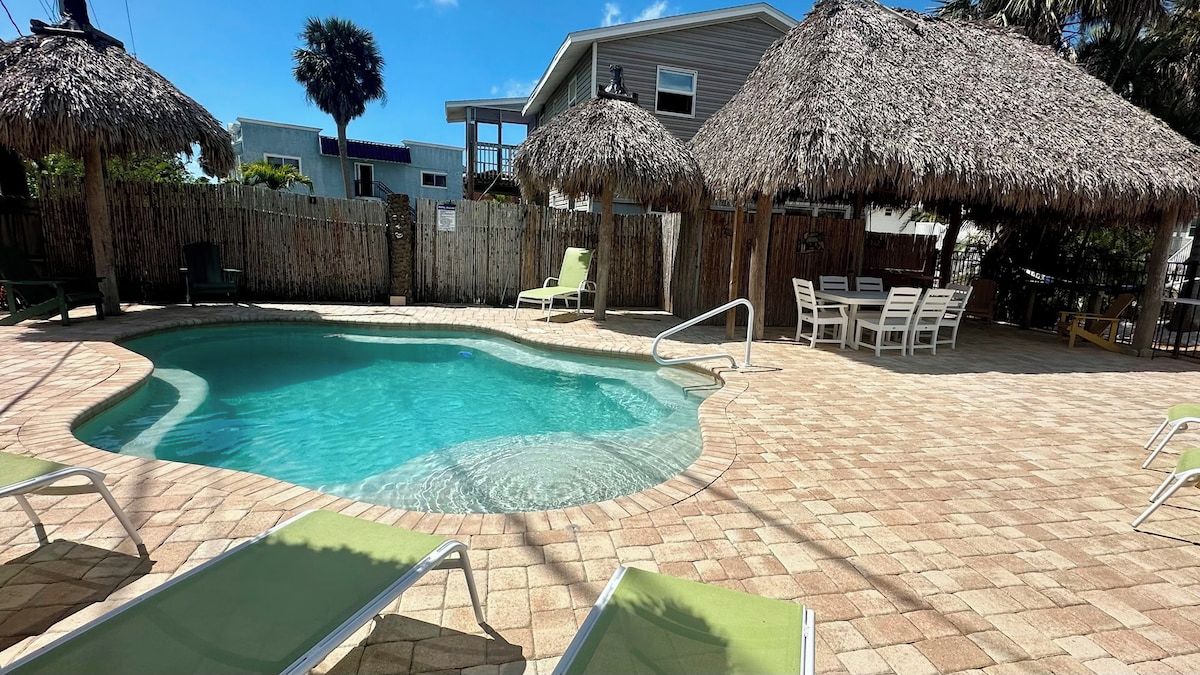 A swimming pool with a curved edge, surrounded by lounge chairs and thatched umbrellas.