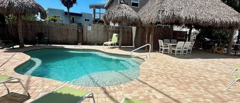 A swimming pool with a curved edge, surrounded by lounge chairs and thatched umbrellas.