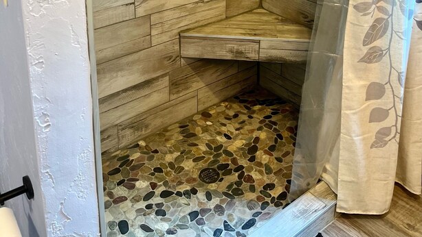 Una ducha con pared de madera, puerta de cristal y cortina de hojas.