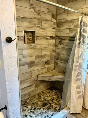 Una ducha con pared de madera, puerta de cristal y cortina de hojas.