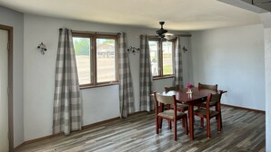 Un comedor con una mesa y sillas de madera, un ventilador de techo y ventanas amplias con cortinas.