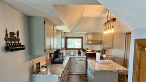 Una cocina moderna con armarios blancos, una isla central, horno empotrado y una lámpara colgante.
