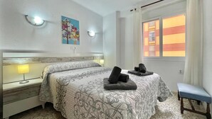 Une chambre d’hôtel avec un lit, des lampes de chevet, un banc et une fenêtre donnant sur des immeubles.
